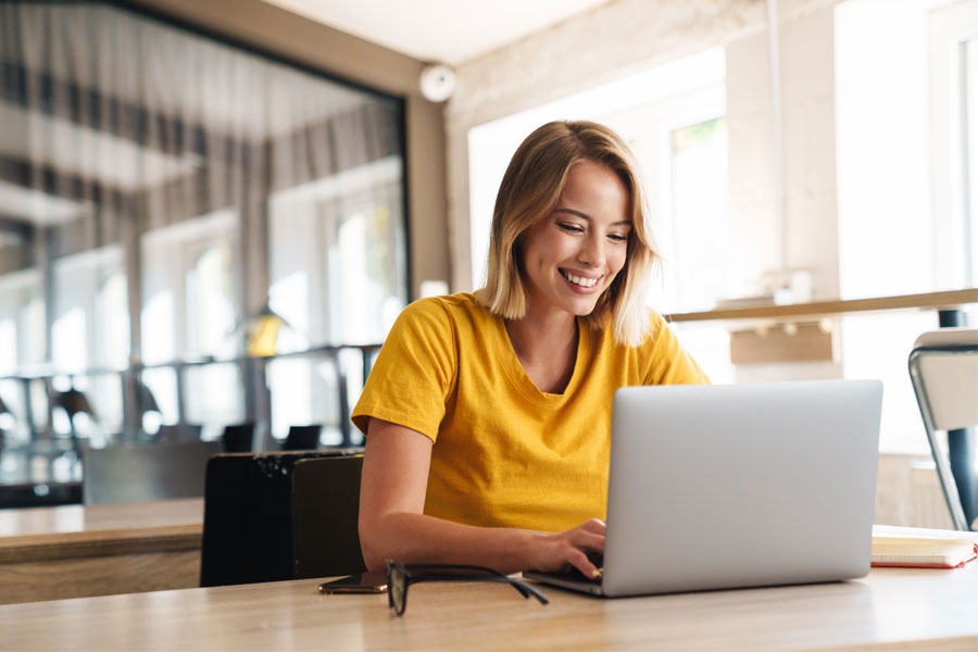 woman in yellow shirt smiling and working on laptop